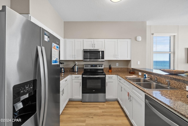 kitchen with light hardwood / wood-style floors, a textured ceiling, sink, white cabinets, and appliances with stainless steel finishes