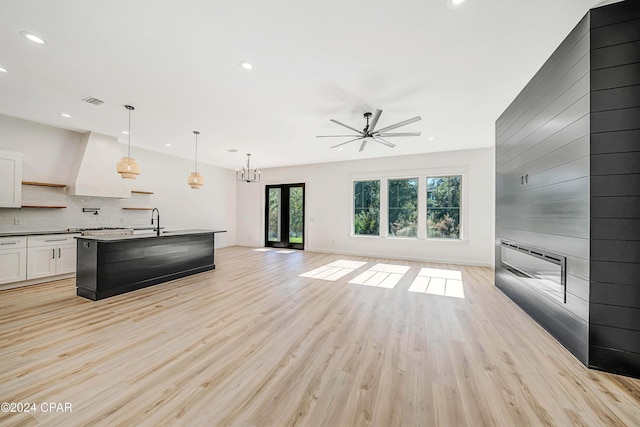 kitchen with ceiling fan with notable chandelier, decorative light fixtures, a center island with sink, light hardwood / wood-style flooring, and white cabinets