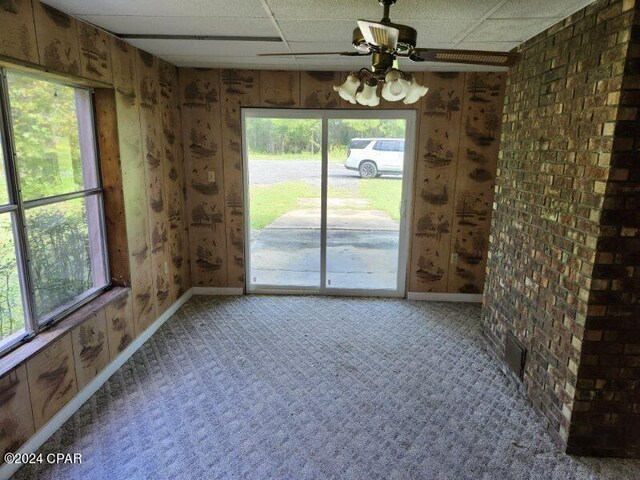 unfurnished dining area with carpet floors, a healthy amount of sunlight, a drop ceiling, and ceiling fan