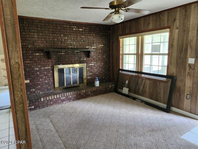 unfurnished living room with ceiling fan, wood walls, a textured ceiling, light carpet, and a fireplace