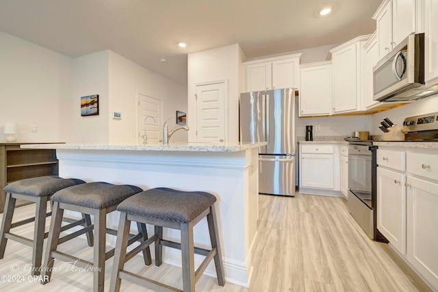 kitchen with white cabinets, light hardwood / wood-style floors, appliances with stainless steel finishes, and a kitchen island with sink