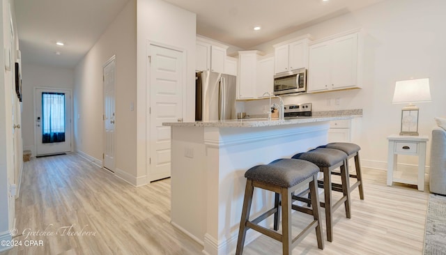 kitchen with white cabinetry, light stone countertops, stainless steel appliances, and a breakfast bar