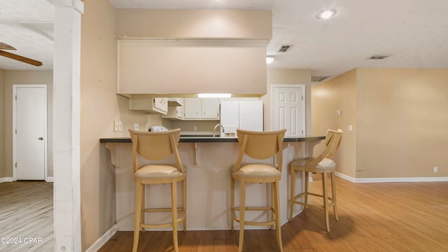 kitchen featuring light hardwood / wood-style floors, white cabinets, kitchen peninsula, white fridge, and ceiling fan