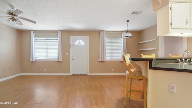 kitchen with ceiling fan, pendant lighting, a textured ceiling, white cabinetry, and light wood-type flooring