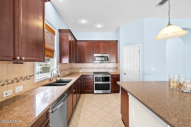 kitchen with sink, decorative backsplash, appliances with stainless steel finishes, decorative light fixtures, and light stone countertops