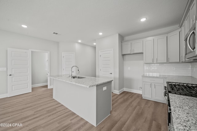 kitchen with light stone countertops, sink, a center island with sink, appliances with stainless steel finishes, and light wood-type flooring