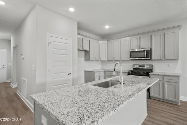 kitchen featuring sink, stainless steel appliances, light stone counters, dark hardwood / wood-style floors, and an island with sink