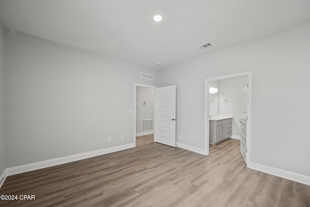 unfurnished bedroom featuring ensuite bath and light hardwood / wood-style floors