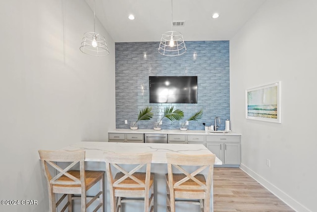 bar featuring sink, light stone countertops, decorative light fixtures, light hardwood / wood-style floors, and white cabinetry