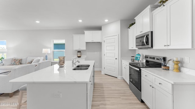 kitchen featuring recessed lighting, appliances with stainless steel finishes, open floor plan, white cabinets, and a sink