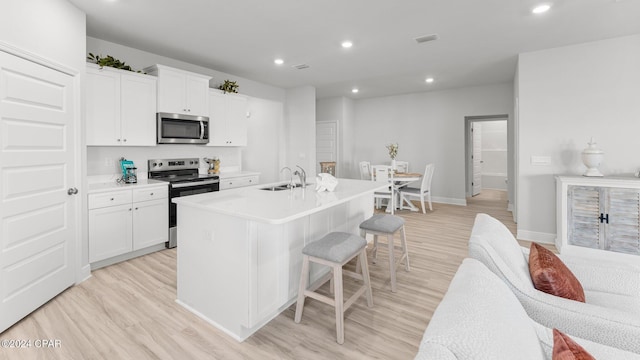 kitchen with a center island with sink, a breakfast bar area, stainless steel appliances, light wood-style floors, and a sink