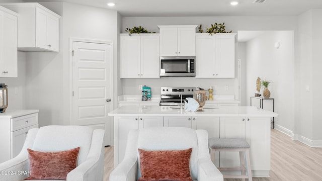 kitchen with appliances with stainless steel finishes, light wood-type flooring, a center island with sink, and white cabinets