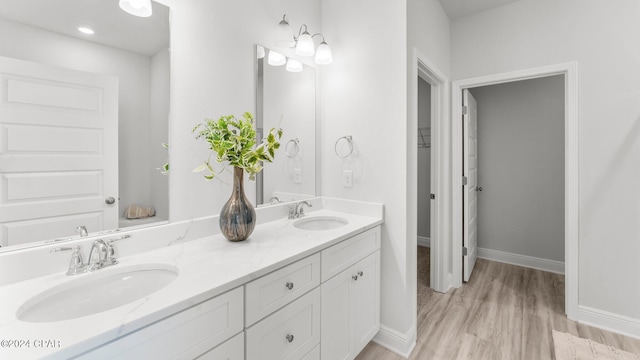 full bath with double vanity, baseboards, a sink, and wood finished floors