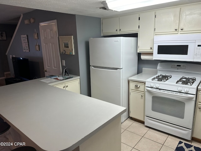 kitchen with cream cabinets, a textured ceiling, light tile patterned floors, and white appliances