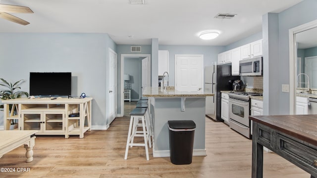 kitchen featuring a kitchen breakfast bar, white cabinets, light hardwood / wood-style floors, and appliances with stainless steel finishes