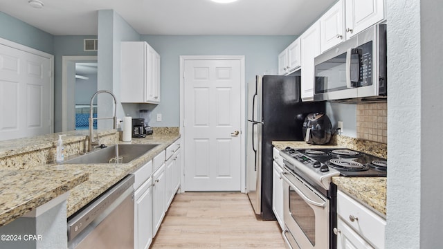 kitchen with light wood-type flooring, sink, white cabinets, stainless steel appliances, and light stone countertops