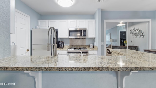 kitchen featuring light stone countertops, white cabinets, appliances with stainless steel finishes, and a kitchen bar