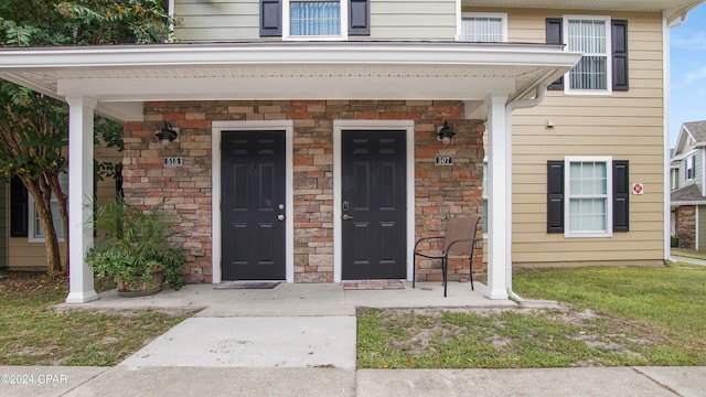 view of exterior entry featuring a lawn and covered porch