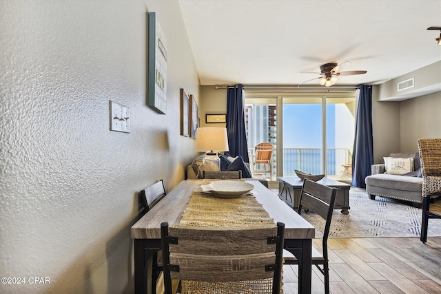 dining area with light wood-style flooring, visible vents, ceiling fan, and a textured wall