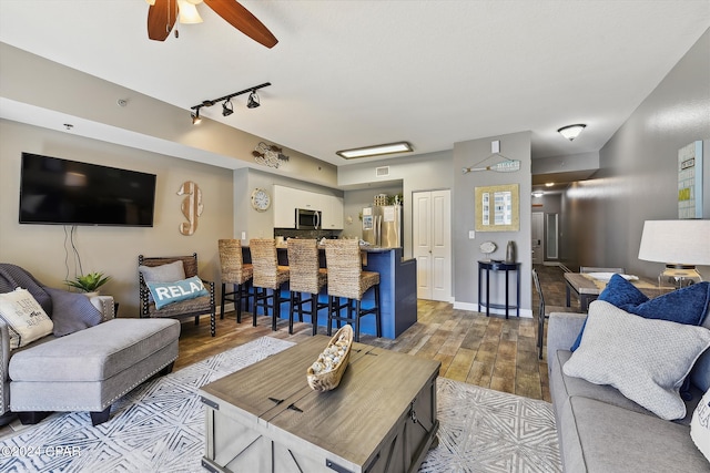 living area featuring baseboards, visible vents, ceiling fan, wood finished floors, and track lighting