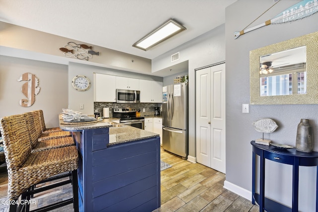 kitchen with decorative backsplash, appliances with stainless steel finishes, a breakfast bar area, a peninsula, and white cabinetry