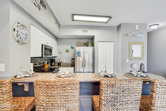 kitchen with visible vents, white cabinets, a breakfast bar area, a peninsula, and stainless steel appliances