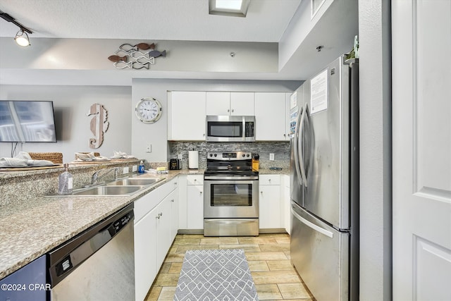 kitchen featuring stainless steel appliances, tasteful backsplash, white cabinetry, a sink, and a peninsula