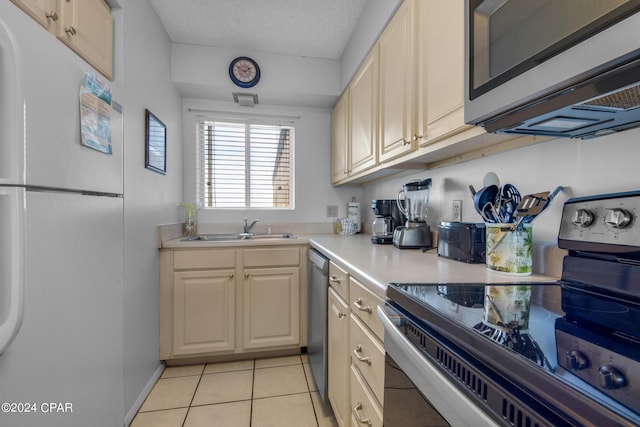 kitchen featuring light tile patterned flooring, stainless steel appliances, cream cabinetry, and sink