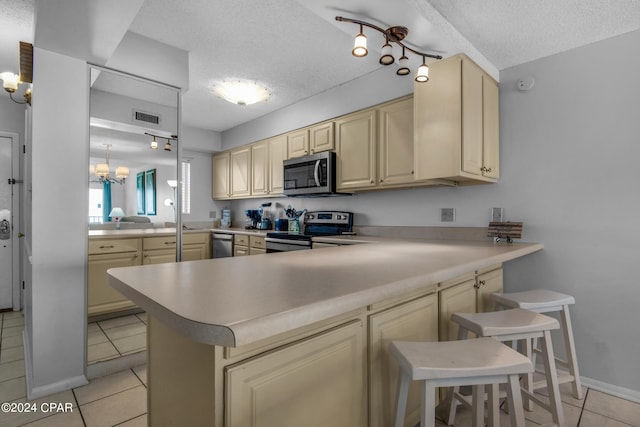 kitchen with a textured ceiling, kitchen peninsula, a kitchen breakfast bar, appliances with stainless steel finishes, and light tile patterned floors