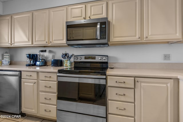 kitchen with light tile patterned flooring, appliances with stainless steel finishes, and cream cabinetry