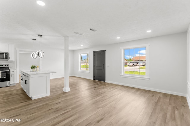 interior space with stainless steel appliances, pendant lighting, light wood-type flooring, white cabinetry, and a textured ceiling