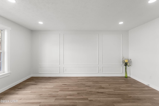 empty room with a wealth of natural light, a textured ceiling, and wood-type flooring