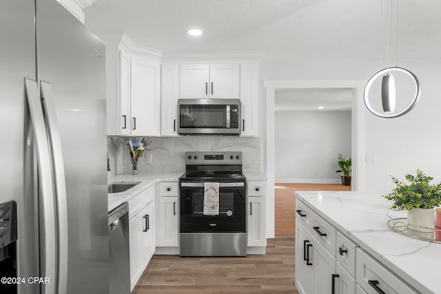 kitchen with appliances with stainless steel finishes, white cabinets, light stone counters, hardwood / wood-style flooring, and decorative backsplash