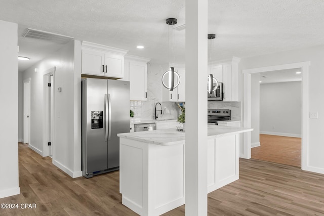 kitchen featuring light wood-type flooring, hanging light fixtures, white cabinetry, stainless steel appliances, and light stone counters