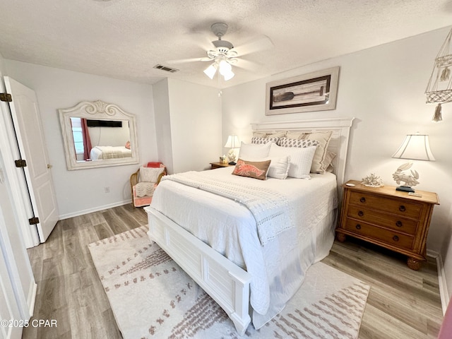 bedroom featuring a textured ceiling, wood finished floors, visible vents, baseboards, and a ceiling fan