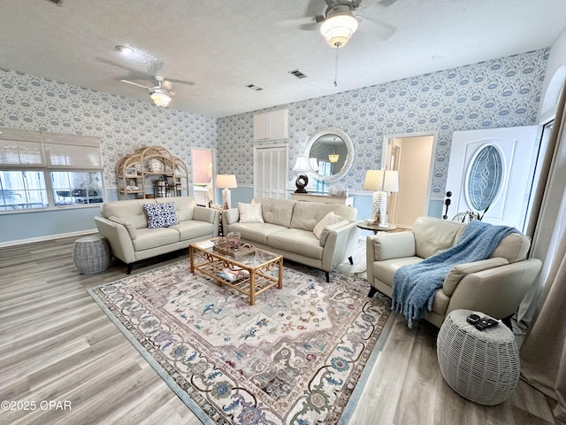 living room with light wood-style floors, ceiling fan, a textured ceiling, baseboards, and wallpapered walls