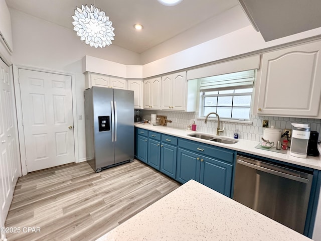 kitchen with light countertops, decorative backsplash, appliances with stainless steel finishes, a sink, and light wood-type flooring