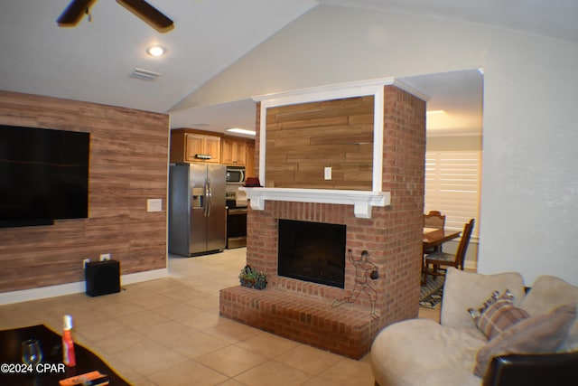 tiled living room featuring a fireplace, wooden walls, ceiling fan, and vaulted ceiling