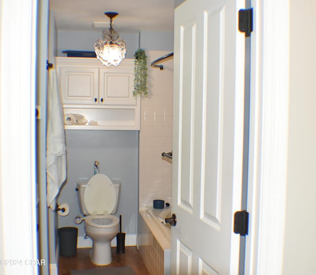 bathroom with tiled shower / bath, toilet, and an inviting chandelier