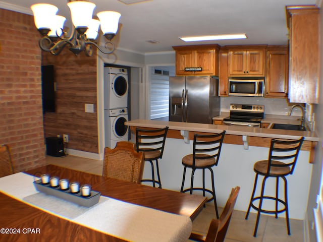 kitchen with sink, appliances with stainless steel finishes, a kitchen bar, stacked washing maching and dryer, and crown molding