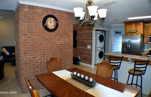 tiled dining space featuring stacked washer / drying machine, wood walls, a chandelier, and ornamental molding