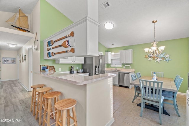 kitchen with white cabinetry, an inviting chandelier, kitchen peninsula, pendant lighting, and appliances with stainless steel finishes