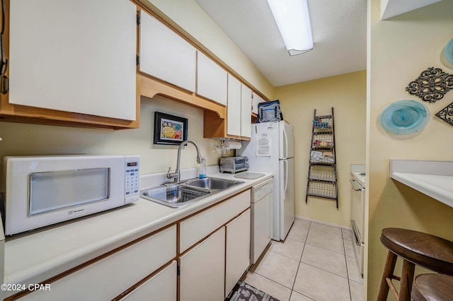 kitchen with sink, white cabinets, white appliances, and light tile patterned floors