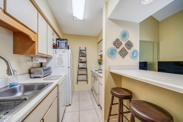 kitchen with white cabinetry, sink, white appliances, a breakfast bar, and light tile patterned flooring