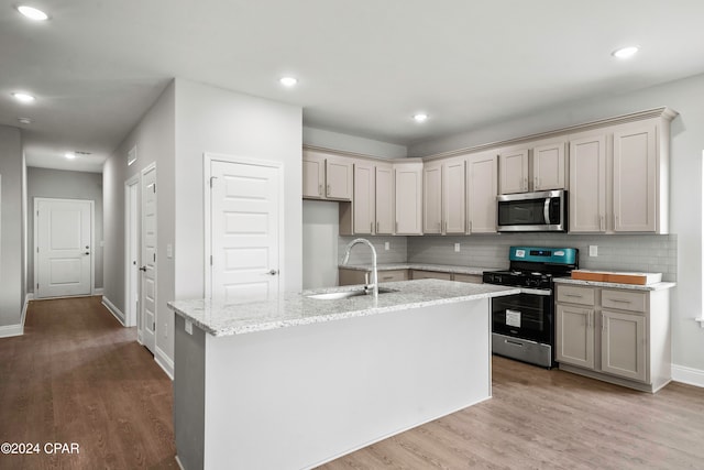 kitchen featuring sink, light stone counters, appliances with stainless steel finishes, an island with sink, and light wood-type flooring