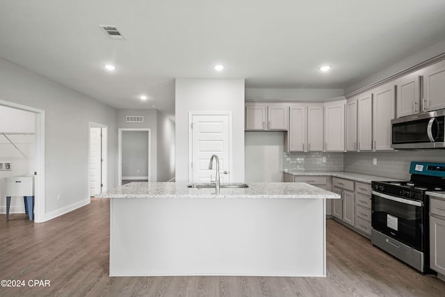 kitchen featuring light stone countertops, appliances with stainless steel finishes, wood-type flooring, and a kitchen island with sink