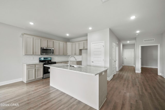 kitchen with backsplash, sink, hardwood / wood-style flooring, light stone countertops, and stainless steel appliances