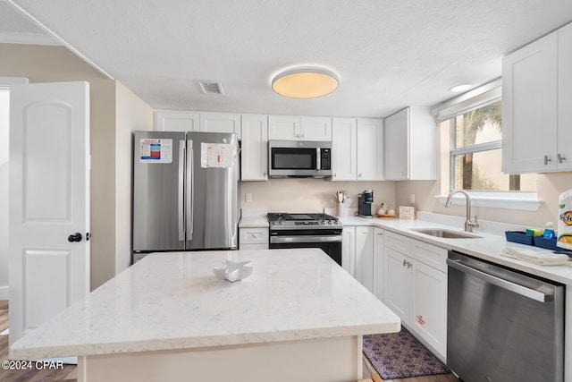 kitchen with appliances with stainless steel finishes, white cabinetry, sink, and a kitchen island