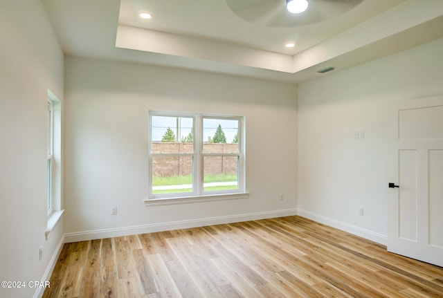 unfurnished room featuring light hardwood / wood-style floors, ceiling fan, and a tray ceiling