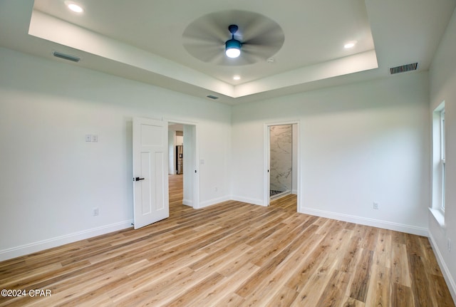 empty room featuring a tray ceiling, ceiling fan, and light hardwood / wood-style flooring